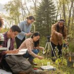 Diverse environmental science students conducting field research outdoors with microscopes and equipment in forest setting